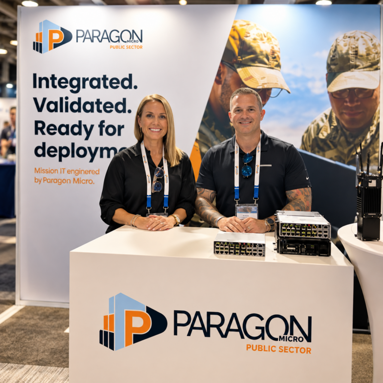 Two Paragon Micro team members at the Paragon Micro Public Sector expo booth, standing behind a branded counter with hardware on display
